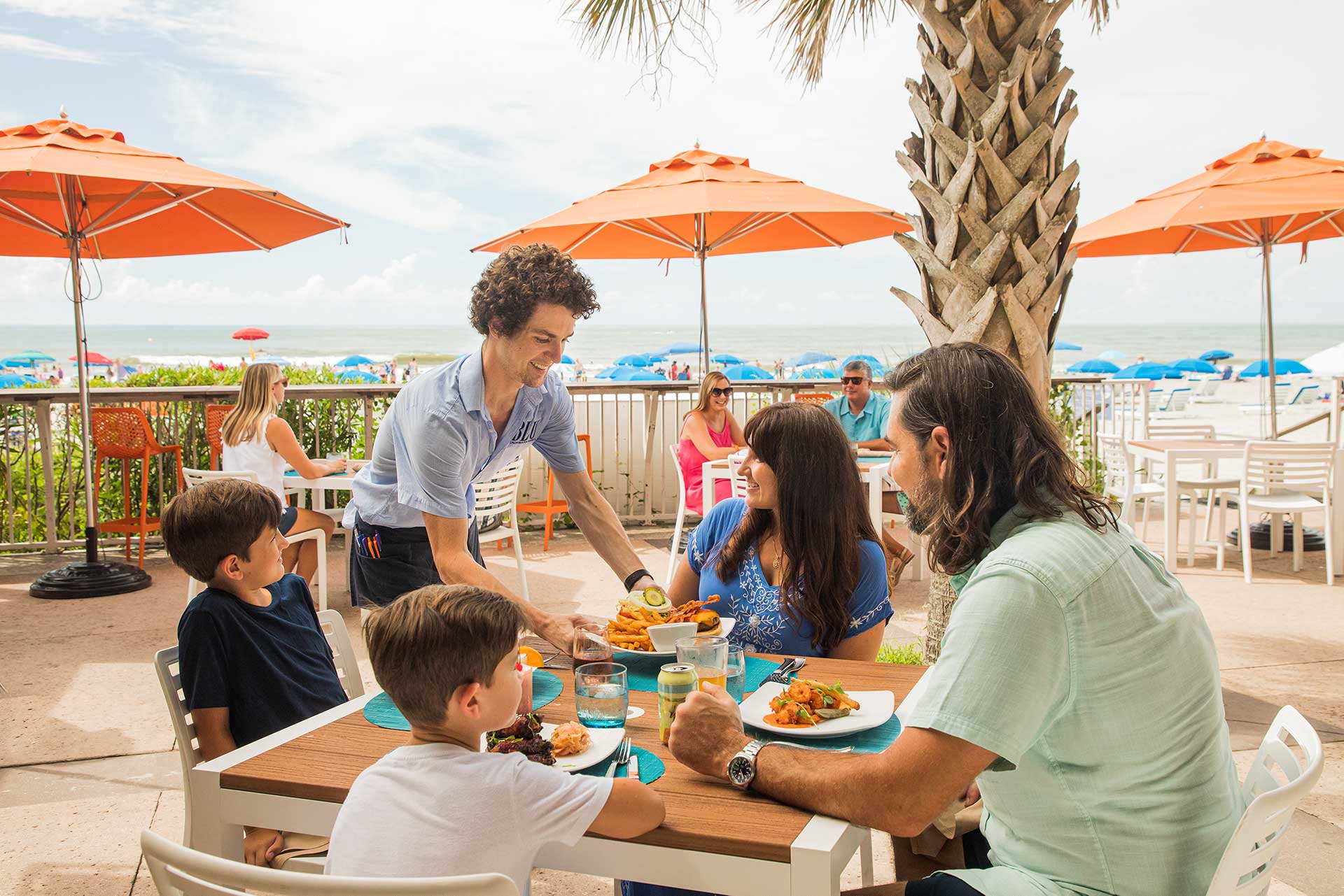 Folly beach oceanfront dining table with server placing dinner plate down for woman and family