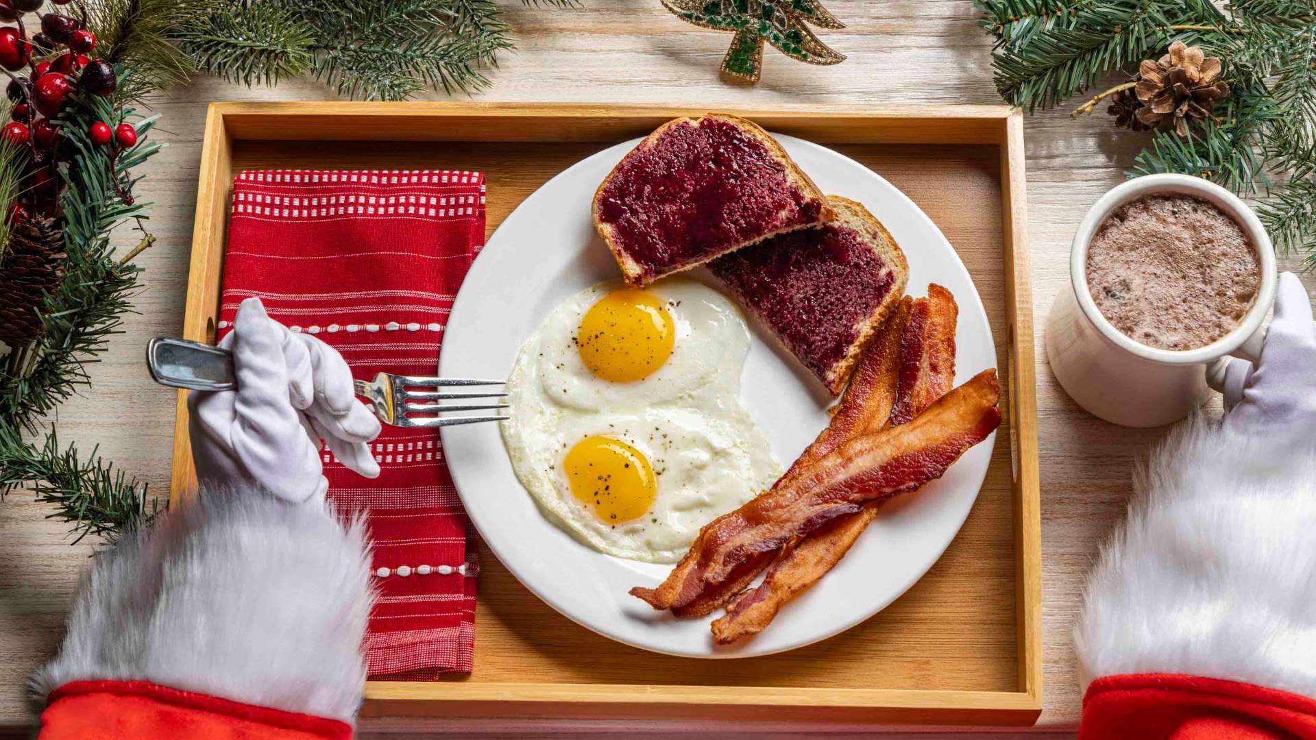 Santa Claus enjoying a plate of bacon, eggs, and toast on a tray.