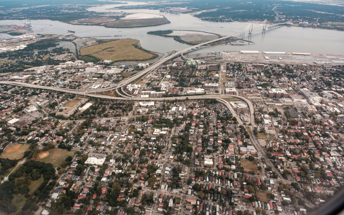 Aerial view of Charleston with residential neighbourhoods, highways, waterways, port facilities, and the Arthur Ravenel Jr. Bridge.