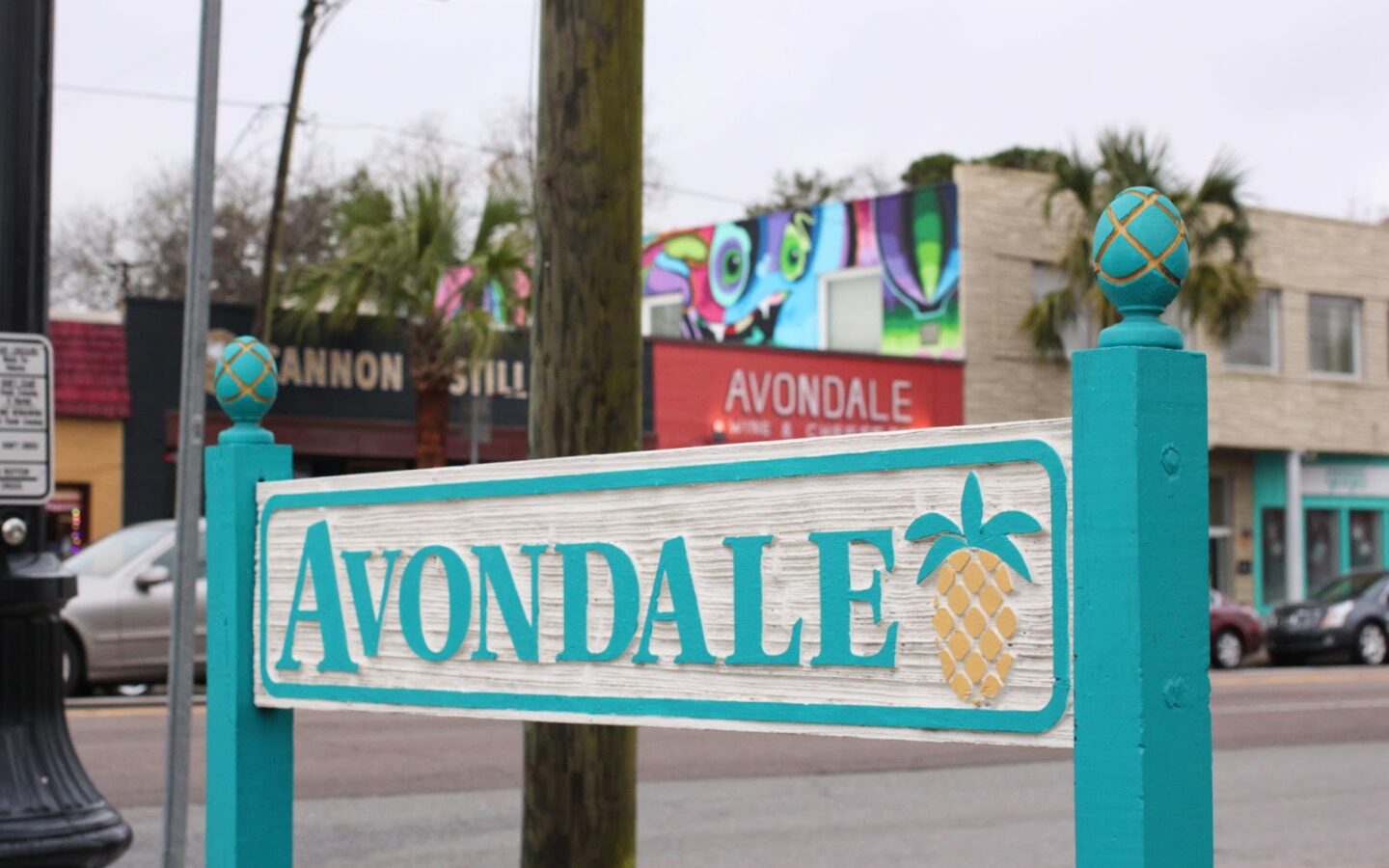 Avondale sign with a pineapple design in front of colourful storefronts and street traffic.