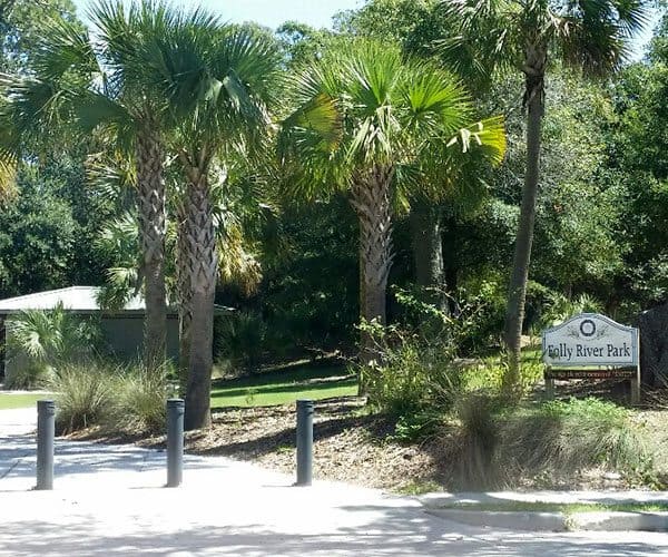Entrance to Folly River Park with palm trees, lush greenery, and a shaded walking path.