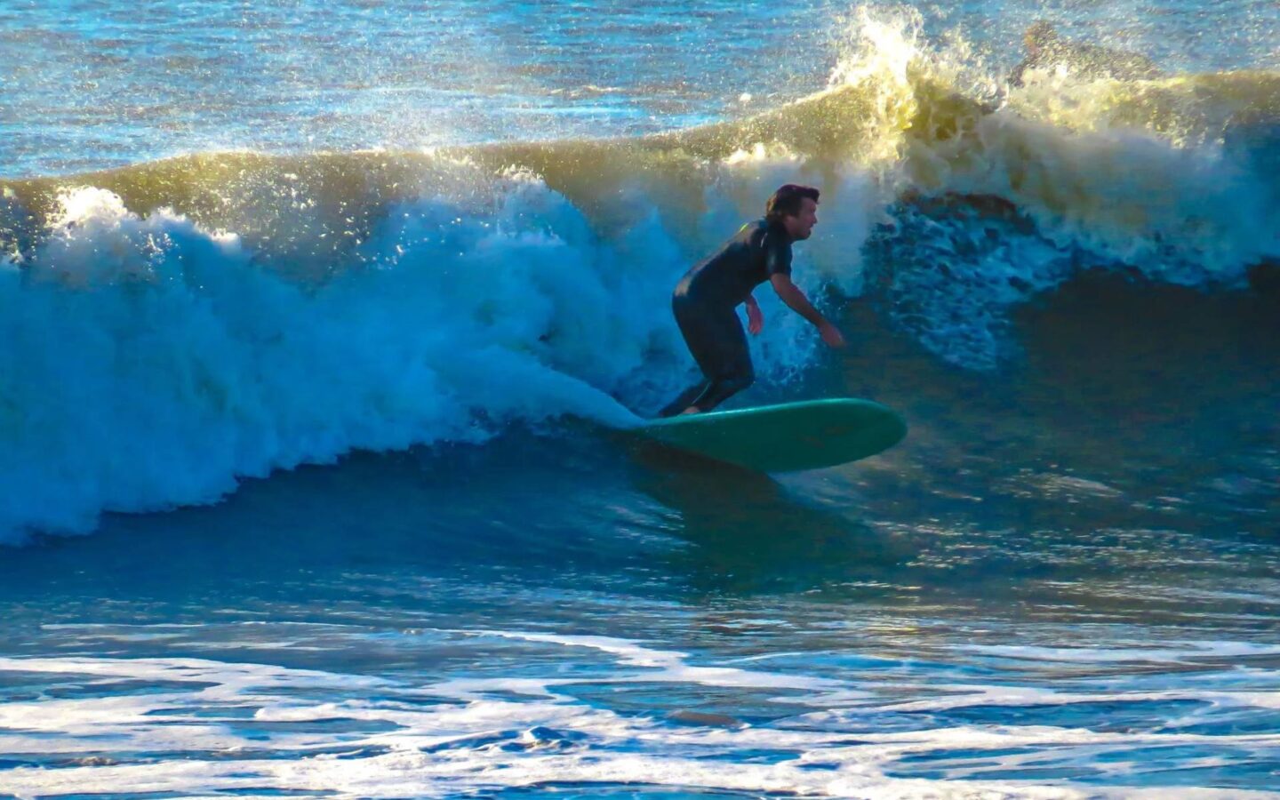Surfer riding a large ocean wave on a teal surfboard.